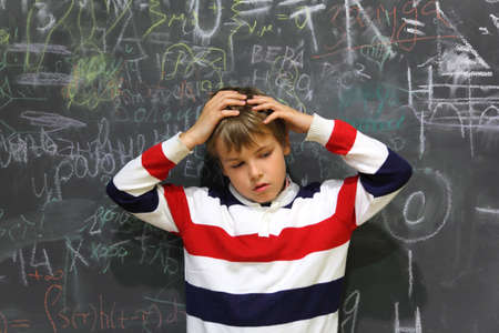 pupil standing near school board and hold on his head half body sad face