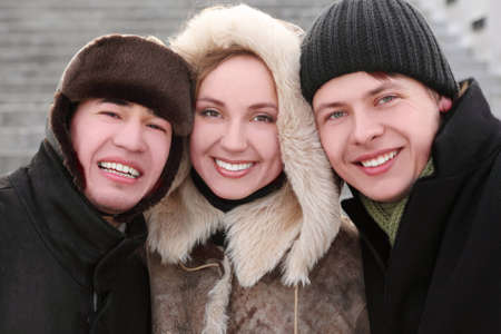 three friends smiling and looking at camera, half body, winter day, stairs on background