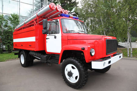Big red fire engine with pipes and flasher on the roof at summer day