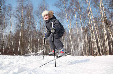 Young boy jumps sideways with cross-country skis and poles inside winter forest at sunny dayの写真素材
