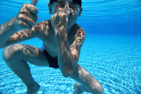 Boy dives under water in  pool and closes  nose  hand and shows  hand of okの写真素材