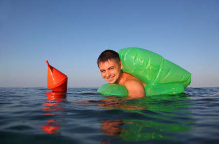  young man swims in sea on green lifeline. orange anchor buoy floats on sea.の写真素材