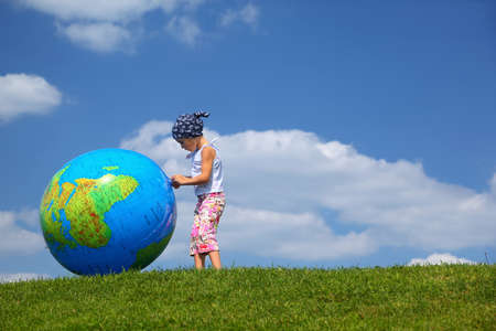 Girl stands on  grass in  day-time and plays with an inflatable globeの写真素材