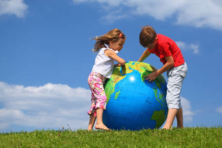 Brother with  sister stand on  grass and study  map on an inflatable globeの写真素材