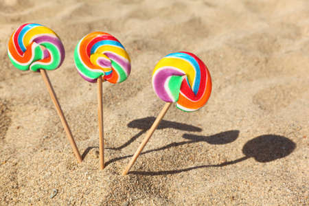 three multicolored lollipops sticked in sand on beach, sunny