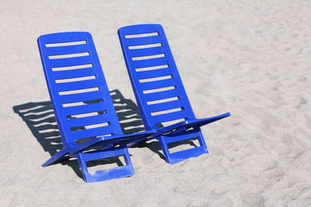 Two empty plastic chairs stand under sunbeams in  day-time on sandの写真素材
