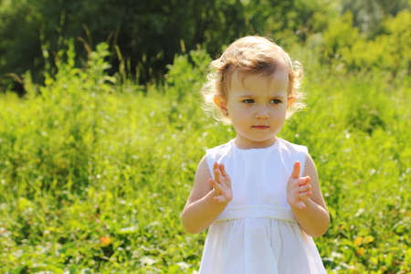 Little girl standing in the grass shows something with her handsの写真素材