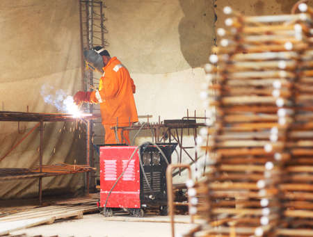 Worker in orange clothes weld metal gratings by acetylene torch