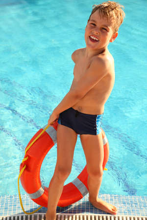 Cheerful little boy pulls out red buoy from the swimming-pool