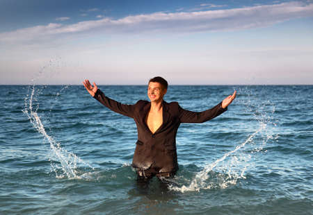 Smiling man in suit stands in sea and splash water at eveningの写真素材