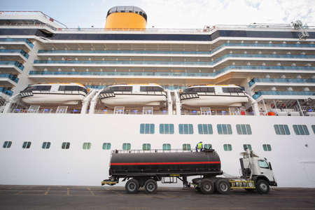 gas-tank truck staying in Qaboos Port. Cruise ship behind truck. man on top of truck.のeditorial素材
