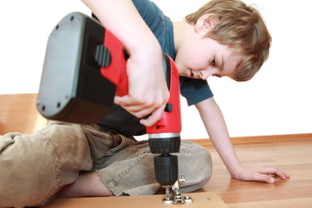Little boy lying on the floor and tightening screws in wooden boardの写真素材