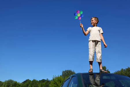 Boy stands on  roof of car and holds  windmill in  handの写真素材