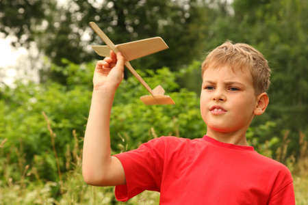 little boy in red T-shirt plays with wooden airplane on nature