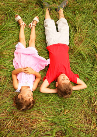 brother in red shirt and sister in pink dress lying on green grass outdoorsの写真素材