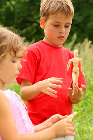 little brother and sister play with wooden little manikins in nature. focus on boyの写真素材