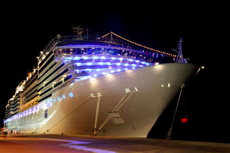 big modern cruise liner with blue lamps standing in dock at night time, mooring with ropes