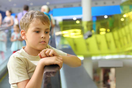 little serious boy standing on escalator and moving up, looking at sideの写真素材