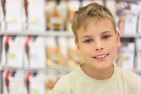 portrait of little caucasian boy smiling and looking at camera, counter in store with commodityの写真素材