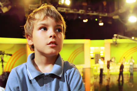 Little boy stands with folded hands in auditorium against the background of television broadcastのeditorial素材