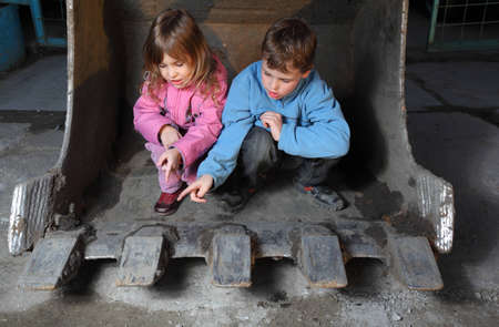 Little girl in pink clothes and boy in blue jacket sitting inside bucket of crawler tractorの写真素材