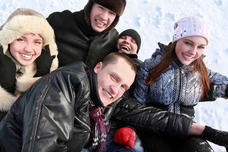Young people by winter day lie on snow in heap and laughの写真素材