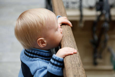 Little boy stands at fencing holding on to banister and looks downwards.の写真素材