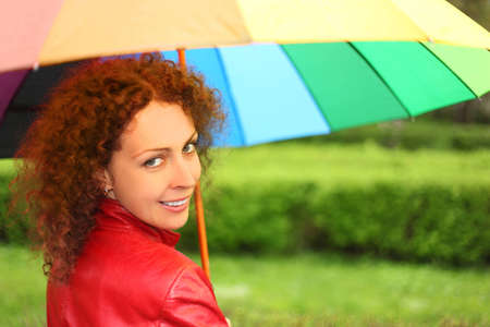 young beauty woman in red jacket with multicolored umbrella looking back and smilingの写真素材