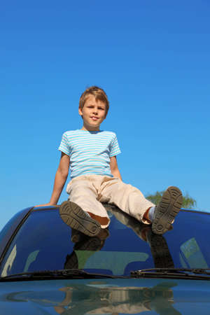 boy sitting on roof of car, blue skyの写真素材