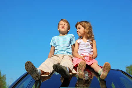 little boy and girl sitting on car roof on blue skyの写真素材