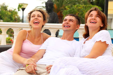 three friends sitting together on couch outdoors and laughing, focus on manの写真素材