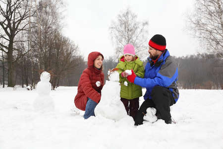 Family from three persons plays in park in winter and sculp snowmanの写真素材