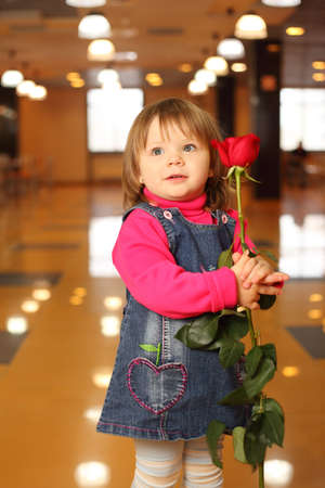 Little beautiful girl with red rose in hands stand in empty cafeの写真素材