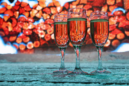 Three glasses of champagne stand near big screen, stack of wood on screen