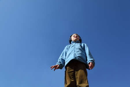 little boy in blue jacket and big black headphones listens to musicの写真素材