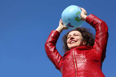 beautiful young woman in red jacket holding balloon in form of globeの写真素材