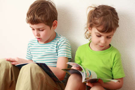 little brother and sister sitting near wall and read children's books, focus on boyの写真素材