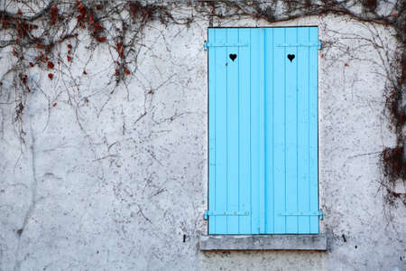 window with blue shutters and white walls, dried ivy, holes in shape of hearts