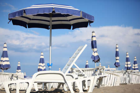many white loungers and blue beach umbrellas on sand at beach. blue sky and clouds. shallow depth of fieldの写真素材