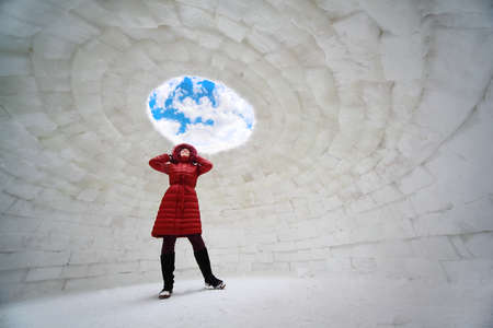 beautiful young woman in red jacket standing inside igloo at winter and looking upの写真素材