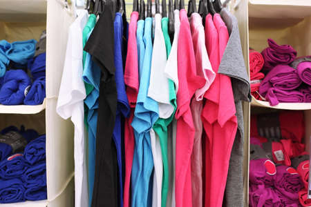Variety of multicolored casual clothes in shop; T-shirts hang on racks and rolled into rolls