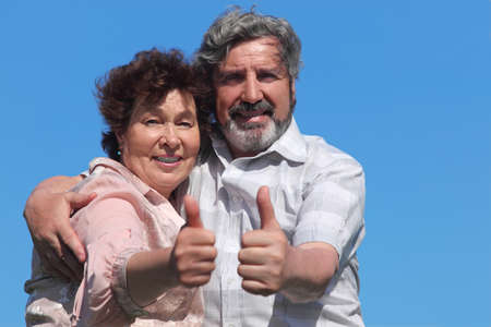 old man and woman making thumbs up gesture and smiling, blue sky