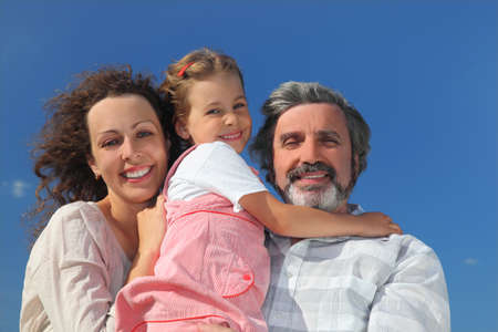 family with girl, mother and grandfather smiling and embracing, blue sky