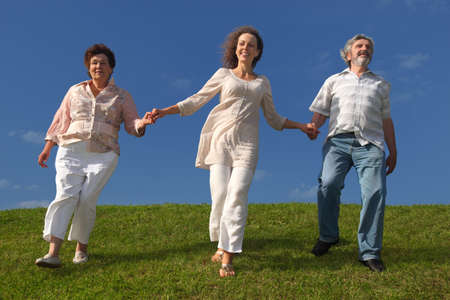 adult daughter and her parents holding for hands, smiling and walking on lawn