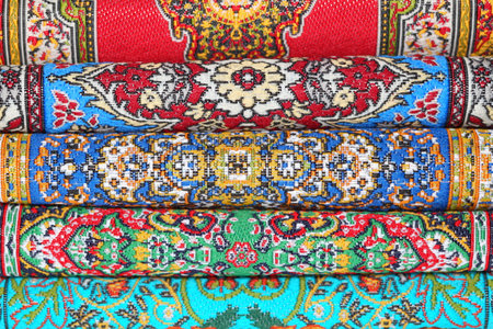 Seven varicoloured carpets lie in rouleau on each other on horizontal line