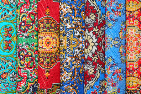 Seven varicoloured carpets lie in rouleau on each other on vertical lineの写真素材