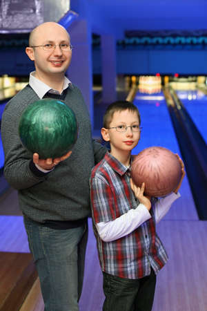 Father and son in glasses stands sideways and holds  balls for bowlingの写真素材