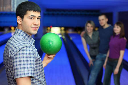 One fellow stands sideways and holds ball for playing in bowling and three friends hearten him, focus on  manの写真素材