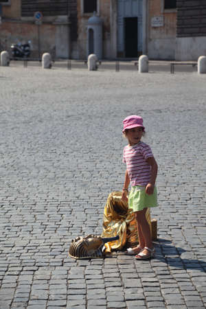 little beautiful girl and fake golden mask of pharaoh on Piazza del Popolo in Rome, Italy