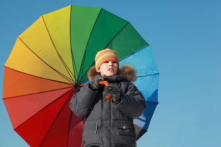 little boy holding big colorful umbrella and looks away at outside in winter